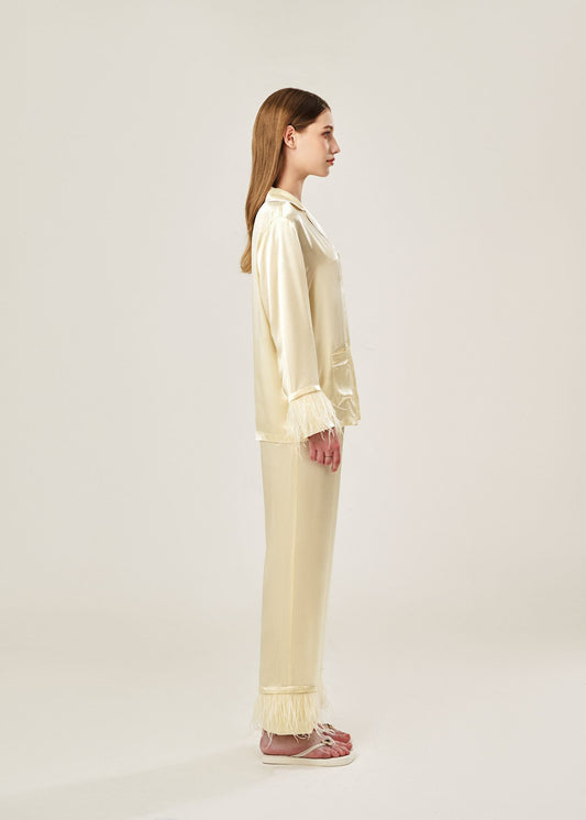 Side view of beige viscose mix rayon pajama set featuring a classic collar, floral buttons, and two front pockets. The detachable ostrich feather trim on the cuffs and pant hems adds a luxurious touch to the relaxed silhouette.