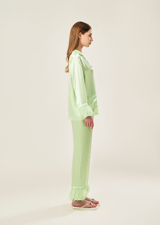 Side view of lime cream viscose mix rayon pajama set featuring a classic collar, floral buttons, and two front pockets. The detachable ostrich feather trim on the cuffs and pant hems adds a luxurious touch to the relaxed silhouette.