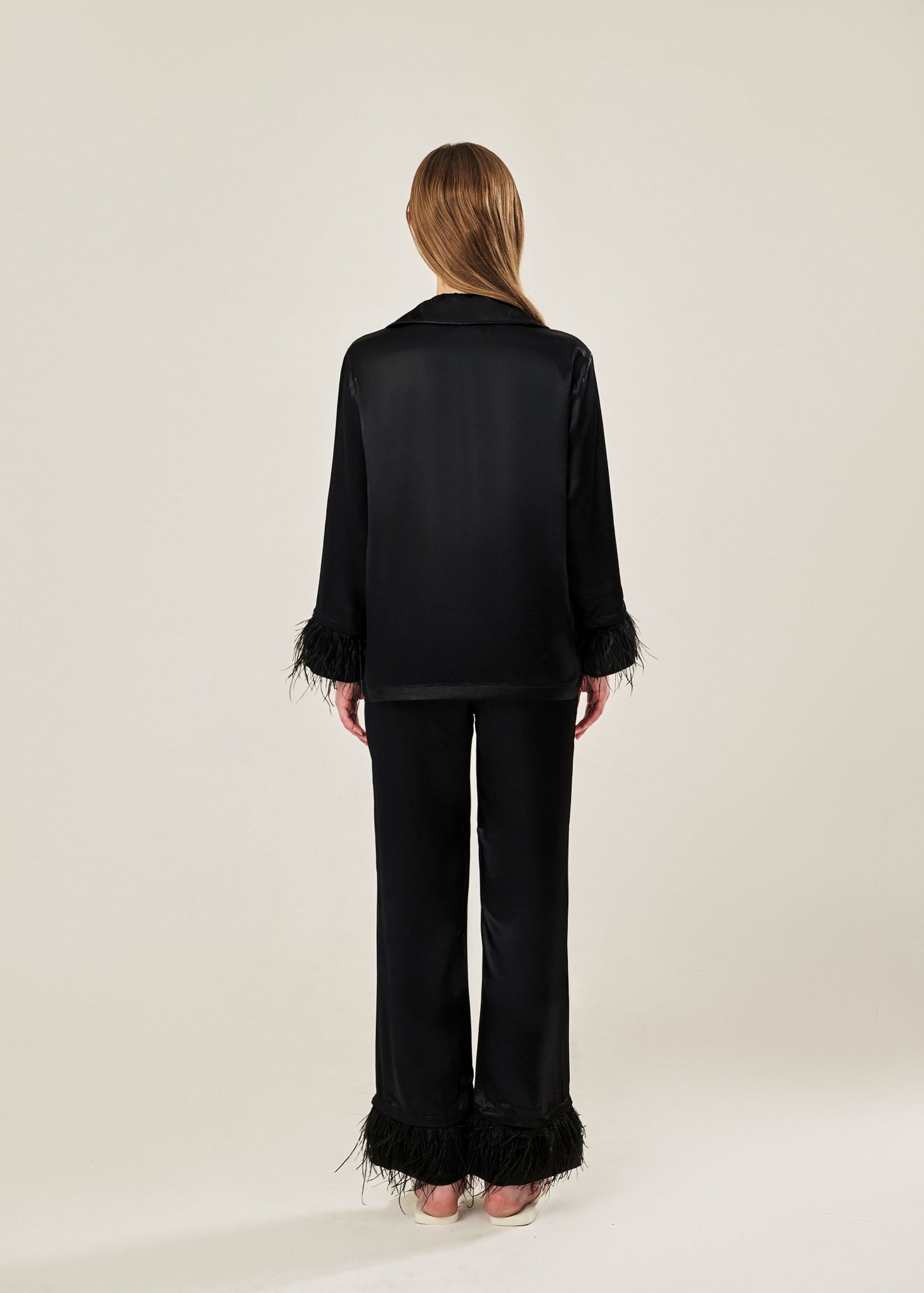 Back view of black viscose mix rayon pajama set featuring a classic collar, floral buttons, and two front pockets. The detachable ostrich feather trim on the cuffs and pant hems adds a luxurious touch to the relaxed silhouette.