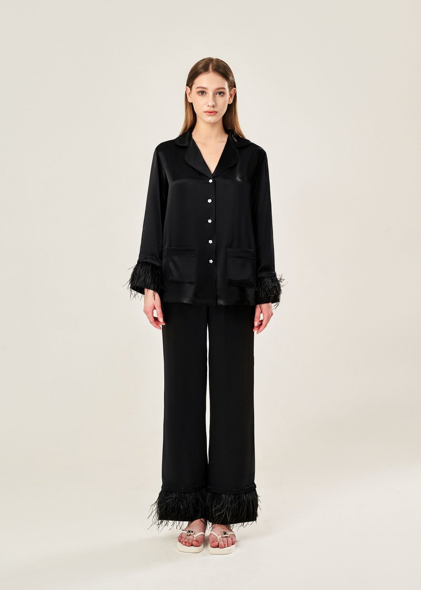 Front view of black viscose mix rayon pajama set featuring a classic collar, floral buttons, and two front pockets. The detachable ostrich feather trim on the cuffs and pant hems adds a luxurious touch to the relaxed silhouette.