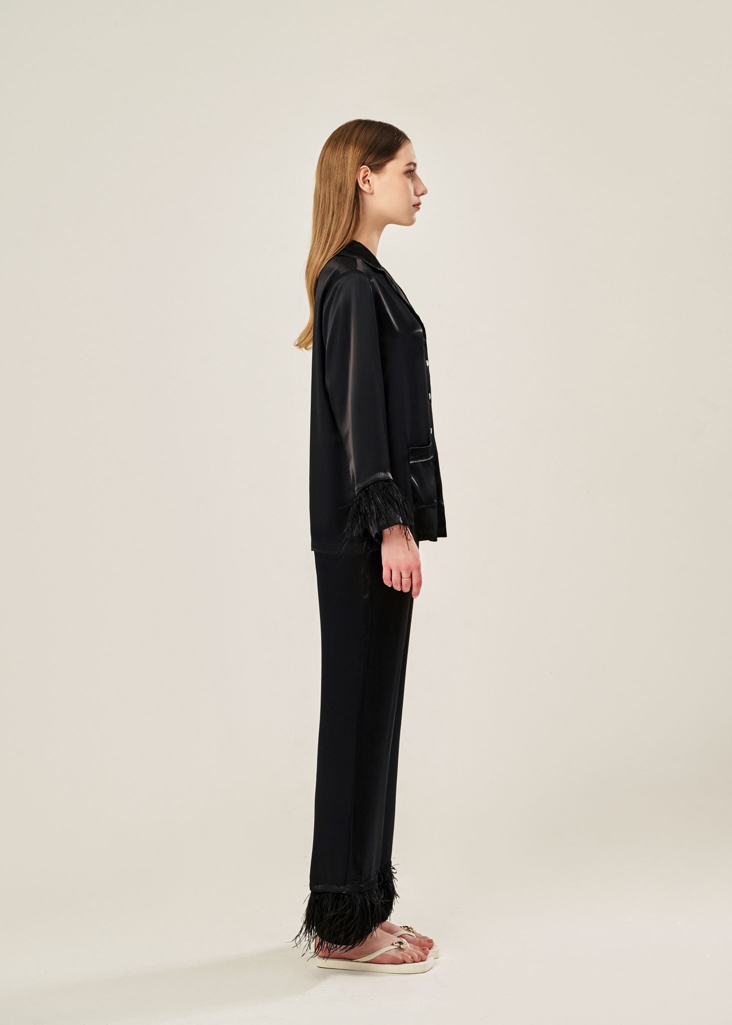 Side view of black viscose mix rayon pajama set featuring a classic collar, floral buttons, and two front pockets. The detachable ostrich feather trim on the cuffs and pant hems adds a luxurious touch to the relaxed silhouette.