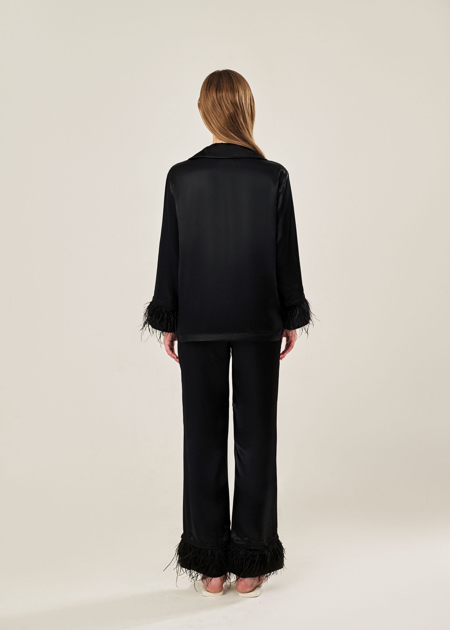 Back view of black viscose mix rayon pajama set featuring a classic collar, floral buttons, and two front pockets. The detachable ostrich feather trim on the cuffs and pant hems adds a luxurious touch to the relaxed silhouette.
