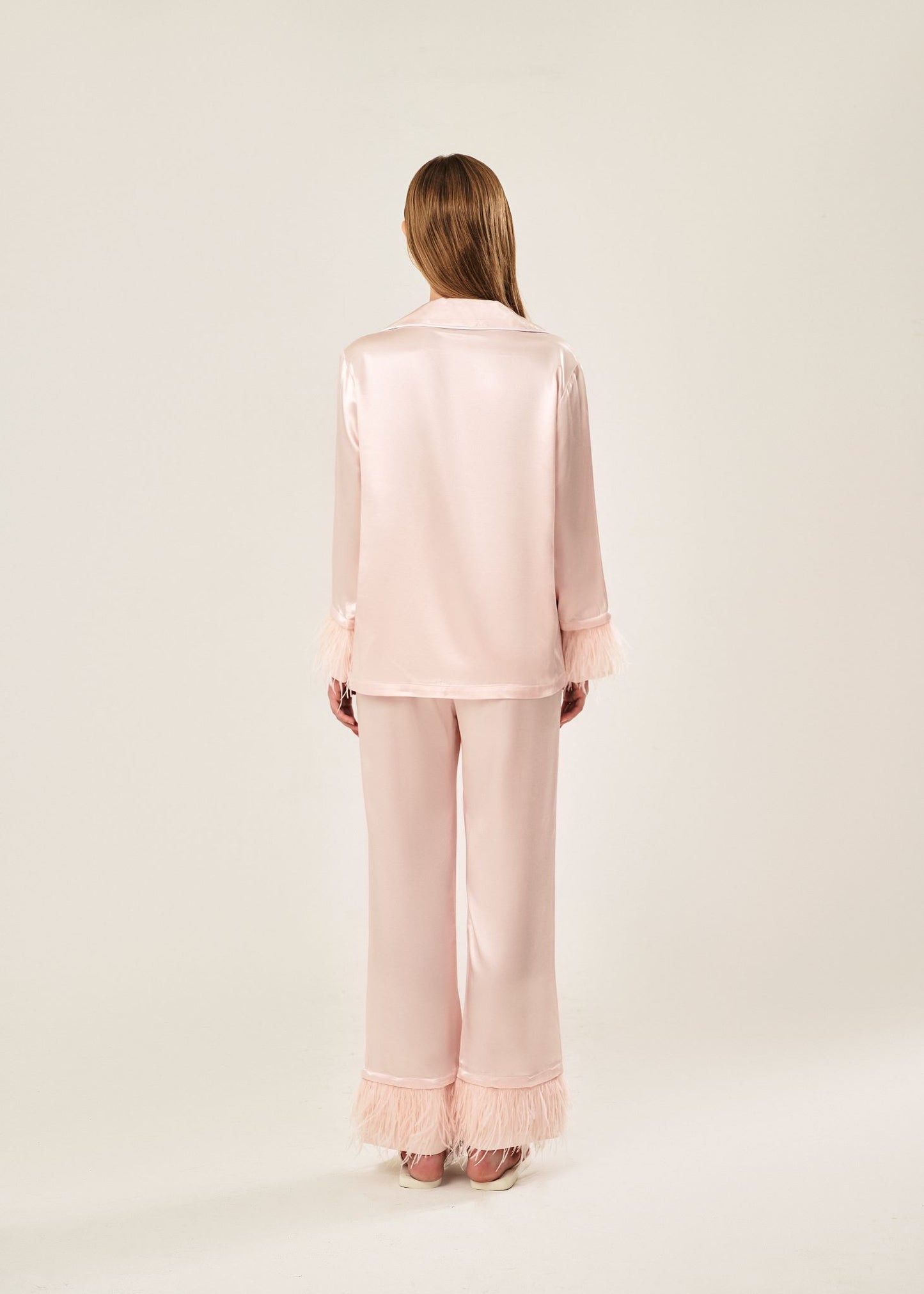 Back view of a blush pink viscose mix rayon pajama set featuring a classic collar, floral buttons, and two front pockets. The detachable ostrich feather trim on the cuffs and pant hems adds a luxurious touch to the relaxed silhouette.