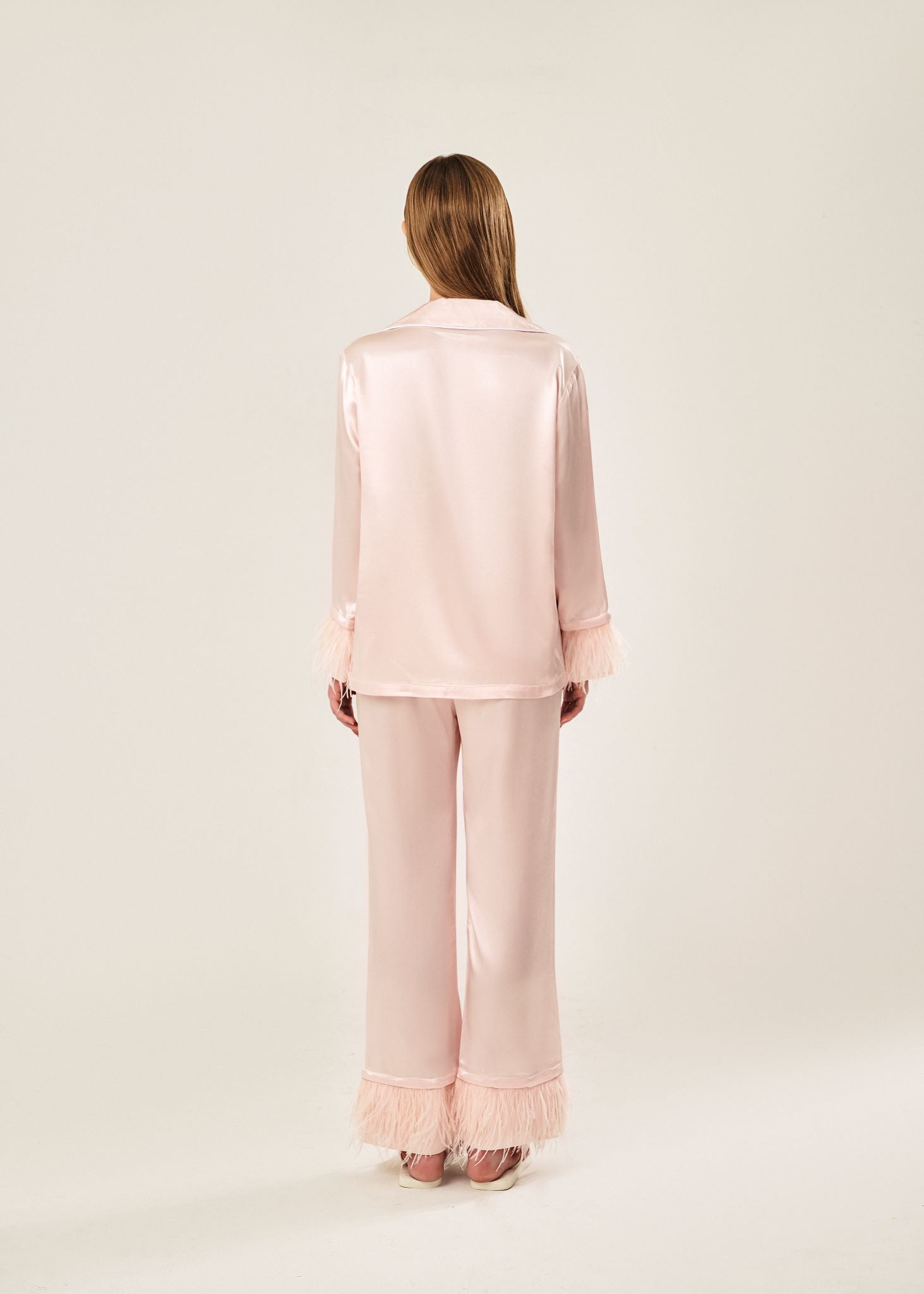 Back view of a blush pink viscose mix rayon pajama set featuring a classic collar, floral buttons, and two front pockets. The detachable ostrich feather trim on the cuffs and pant hems adds a luxurious touch to the relaxed silhouette.