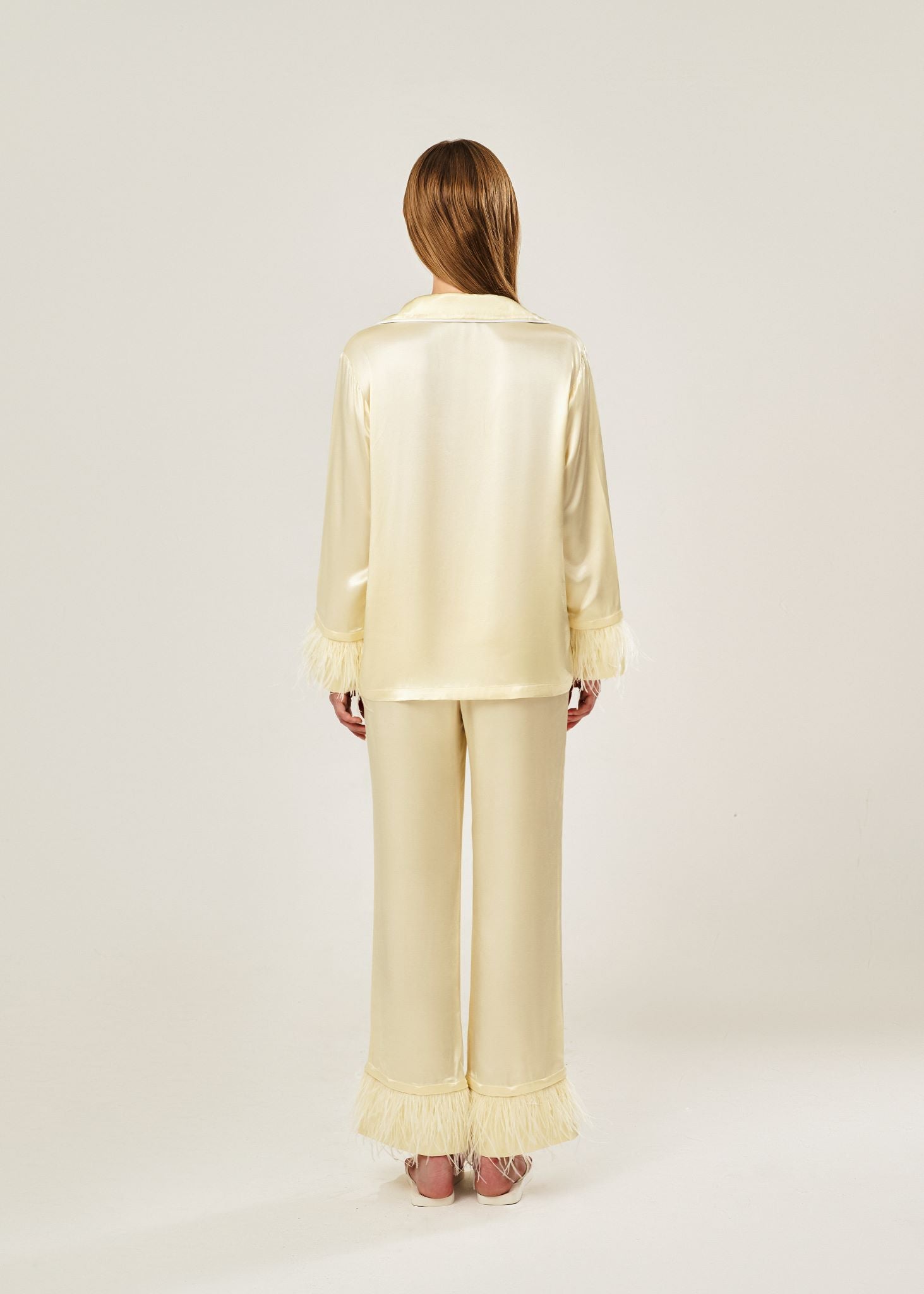 Back view of beige viscose mix rayon pajama set featuring a classic collar, floral buttons, and two front pockets. The detachable ostrich feather trim on the cuffs and pant hems adds a luxurious touch to the relaxed silhouette.