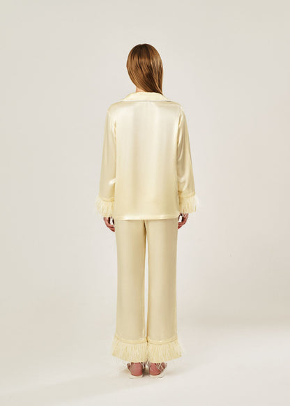 Back view of beige viscose mix rayon pajama set featuring a classic collar, floral buttons, and two front pockets. The detachable ostrich feather trim on the cuffs and pant hems adds a luxurious touch to the relaxed silhouette.