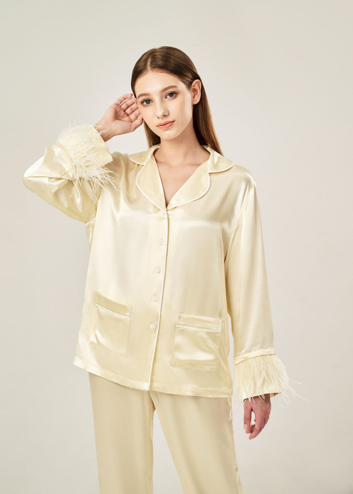 Detail view of beige viscose mix rayon pajama set featuring a classic collar, floral buttons, and two front pockets. The detachable ostrich feather trim on the cuffs and pant hems adds a luxurious touch to the relaxed silhouette.
