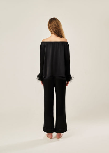 Back view of a black off-shoulder pajama set in soft viscose with a silky feel, featuring a delicate bow detail on the neckline and waistband. Detachable ostrich feather trim on the sleeves adds a chic, elegant finish to the relaxed silhouette.