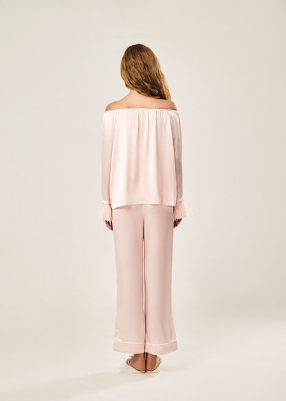 Back view of a blush pink off-shoulder pajama set in soft viscose with a silky feel, featuring a delicate bow detail on the neckline and waistband. Detachable ostrich feather trim on the sleeves adds a chic, elegant finish to the relaxed silhouette.
