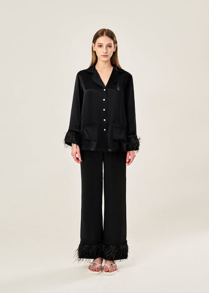Front view of black viscose mix rayon pajama set featuring a classic collar, floral buttons, and two front pockets. The detachable ostrich feather trim on the cuffs and pant hems adds a luxurious touch to the relaxed silhouette.
